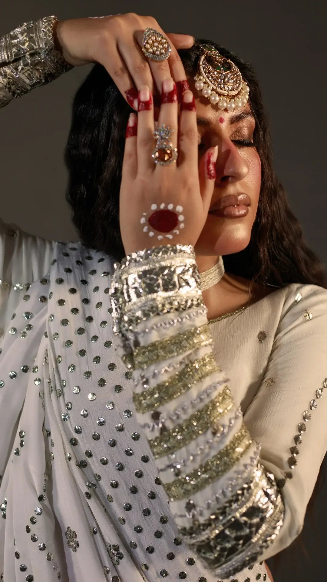 Woman in traditional attire with jewelry and makeup, focusing on hand and face.