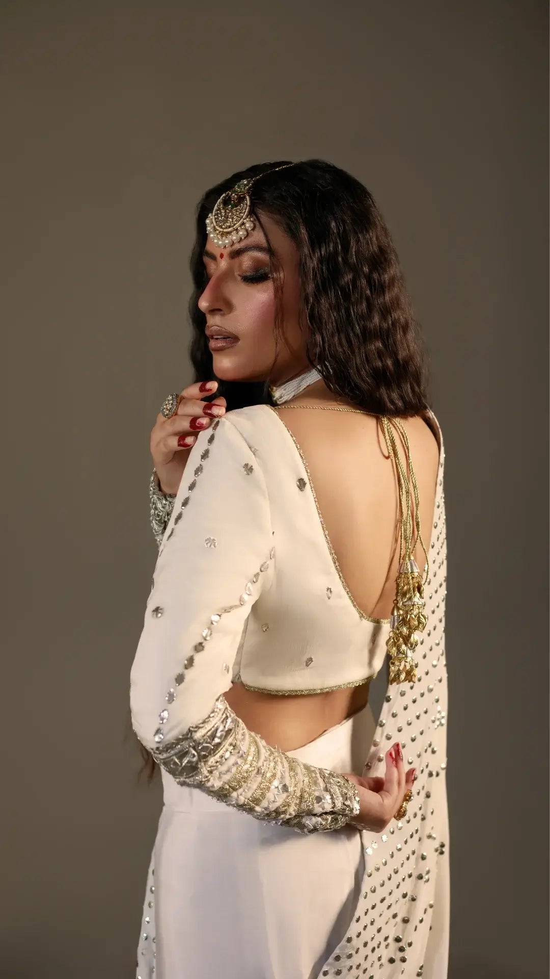 Woman in a white saree with gold detailing against a plain background