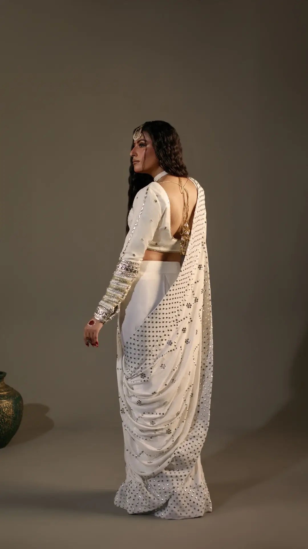 Woman in a white saree with intricate patterns against a plain background