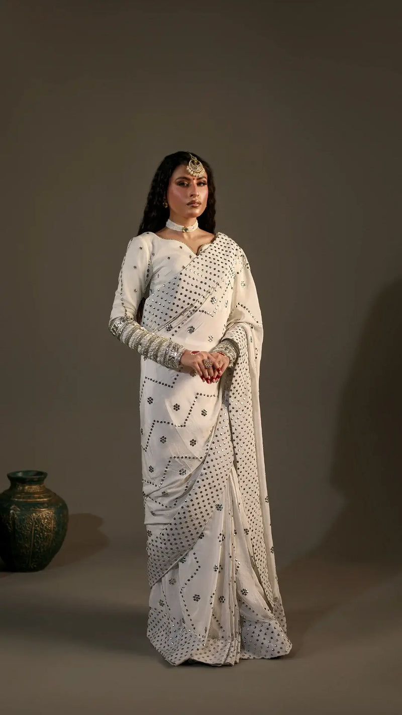 Woman in a white saree with black patterns against a plain background