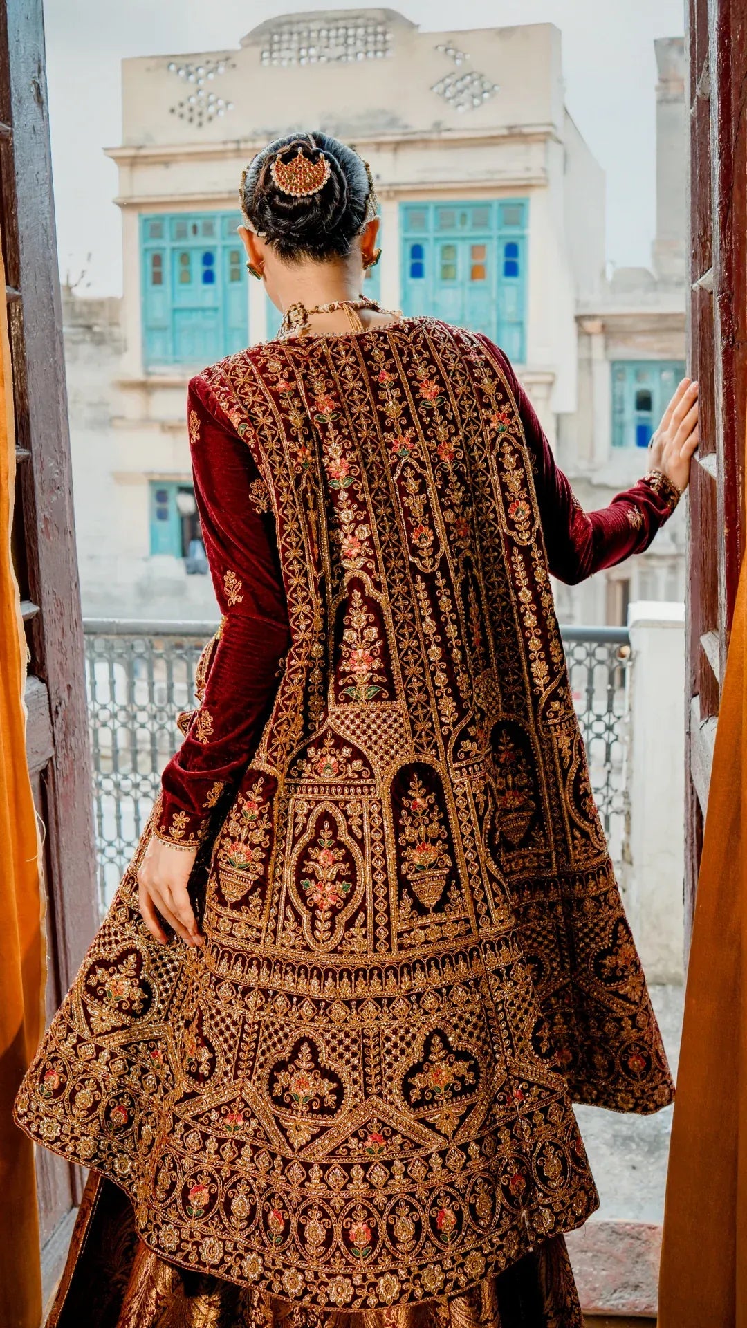 Person wearing a traditional embroidered outfit with a decorative backdrop