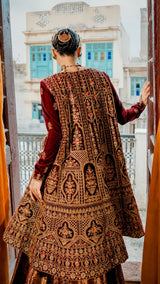Person wearing a traditional embroidered outfit with a decorative backdrop
