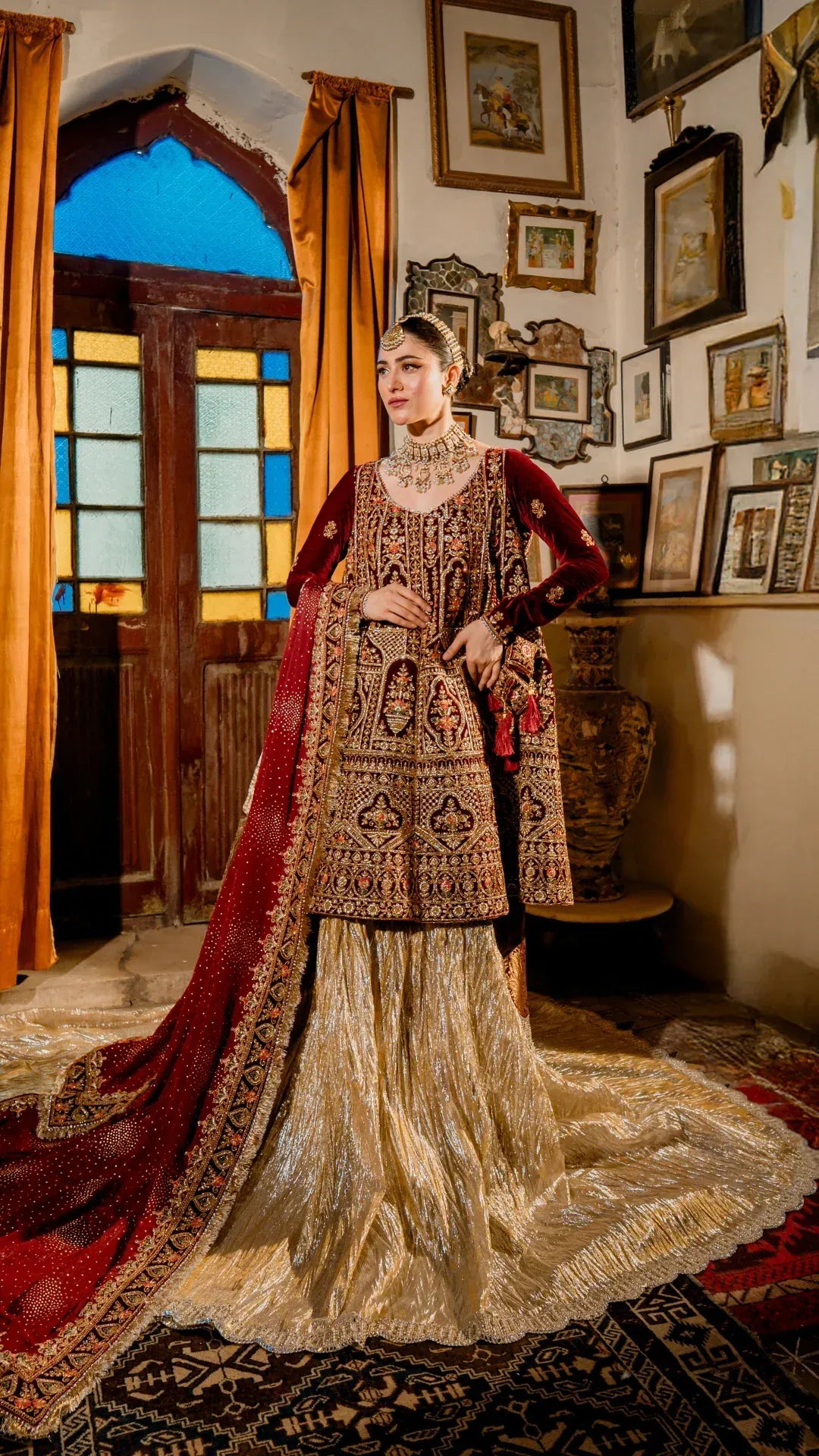 Woman in traditional embroidered outfit with red dupatta in a decorated room.