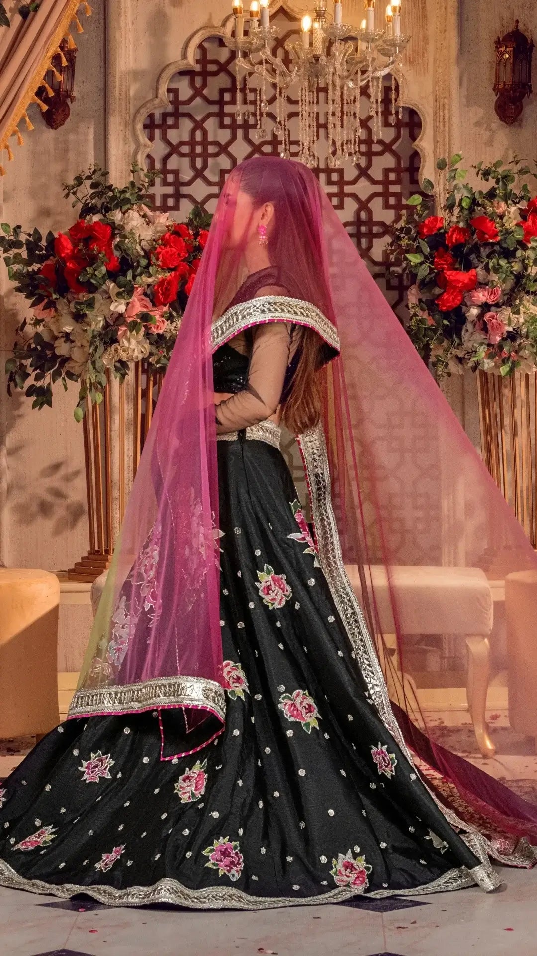 Black embroidered traditional outfit with a pink dupatta in a decorated indoor setting