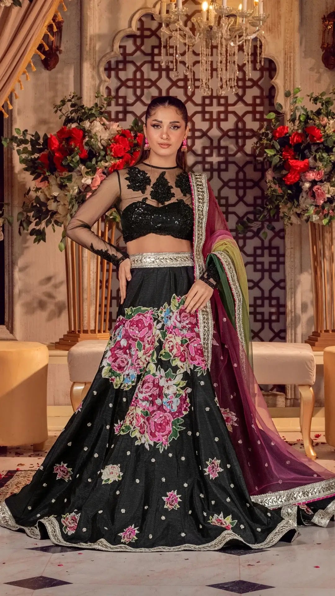 Woman in a black embroidered traditional outfit with floral patterns in a decorated indoor setting.