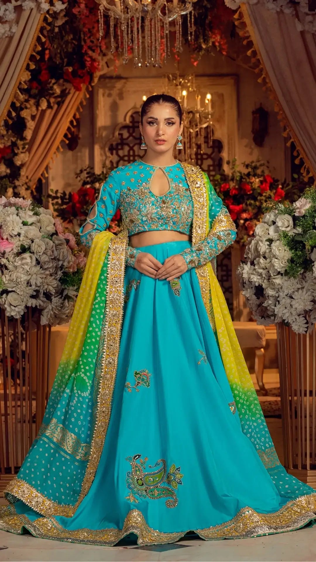 Woman in turquoise embroidered lehenga with gold accents and dupatta, wedding floral decor
