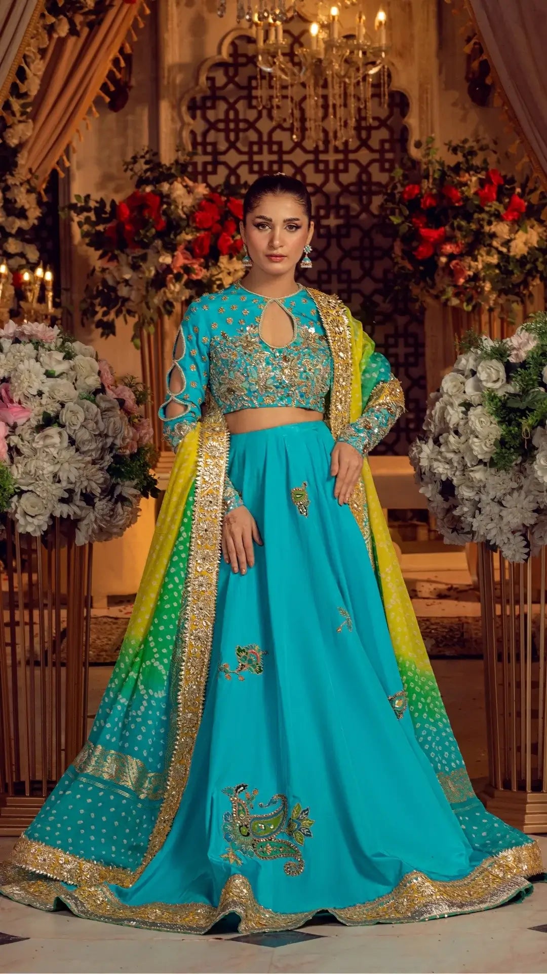 Woman in a traditional turquoise and yellow outfit with floral decorations in the background