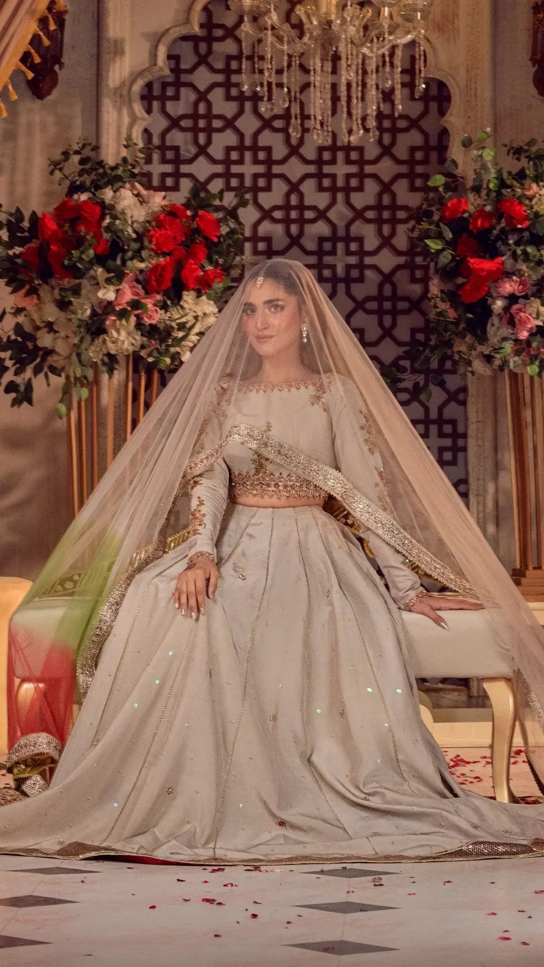 Woman in ivory embellished bridal dress and veil, seated in a floral, elegant setting