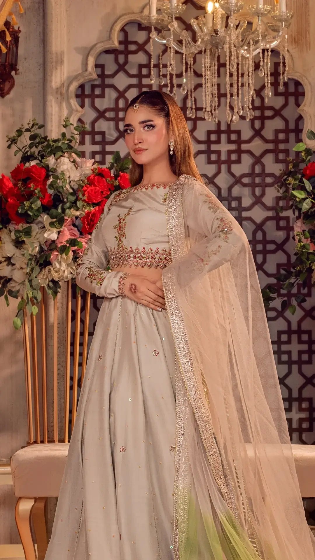 Woman in a traditional outfit with floral decorations and intricate patterns in the background