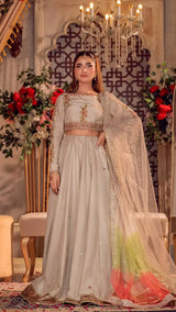 Woman in an elegant ivory Pakistani formal dress with floral embroidery and net dupatta, styled for a wedding or party, standing in a lavish indoor setting with chandeliers and floral decor.