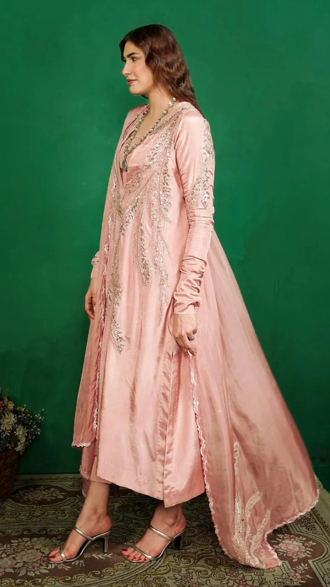 Woman wearing a pink embroidered traditional outfit against a green background