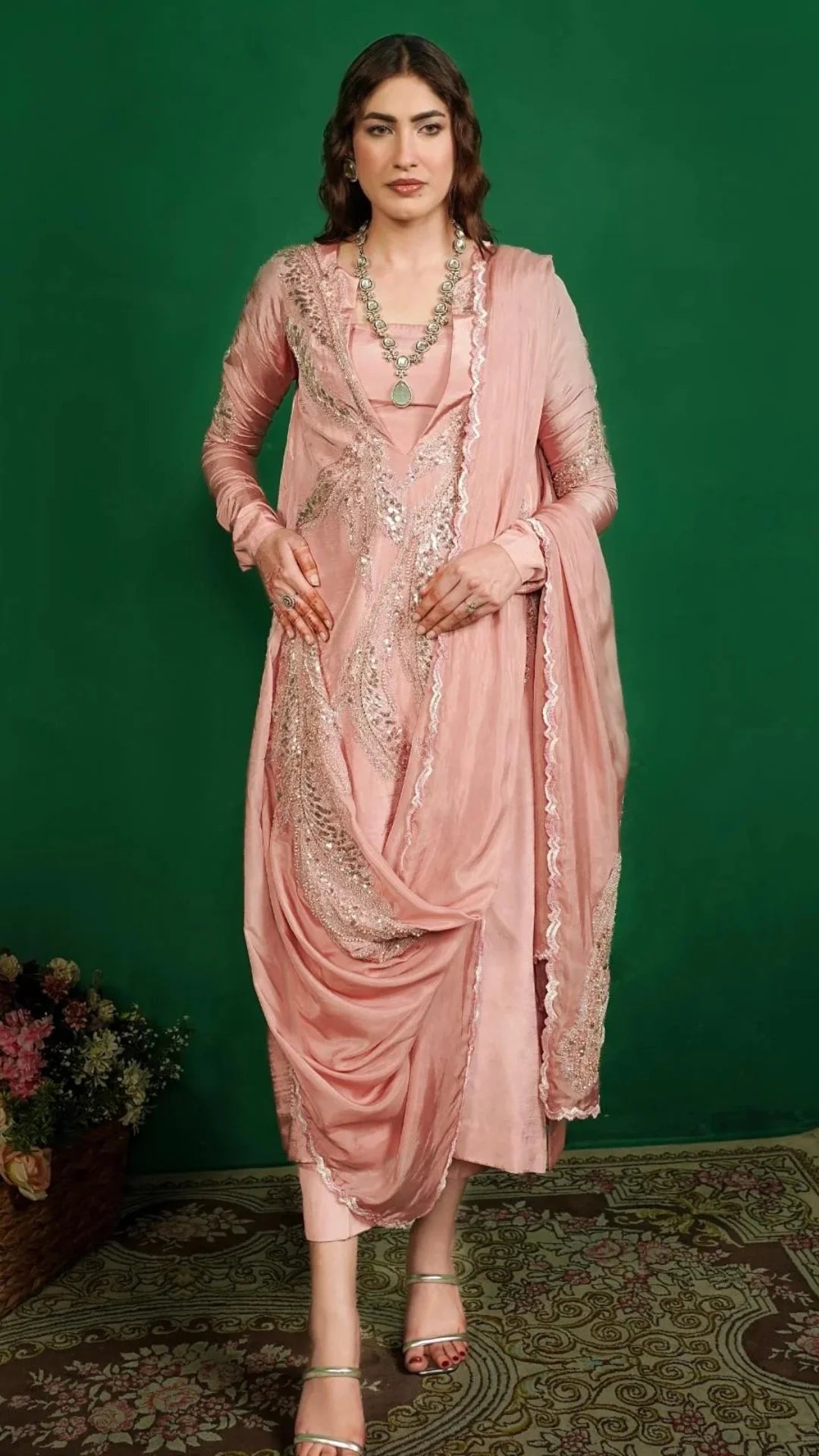 Woman in a pink saree with intricate designs against a green background
