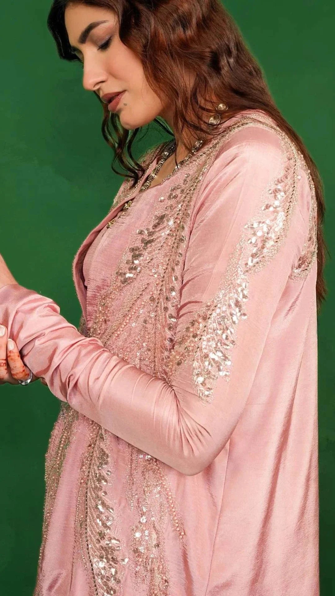 Woman wearing a pink embroidered traditional outfit against a green background