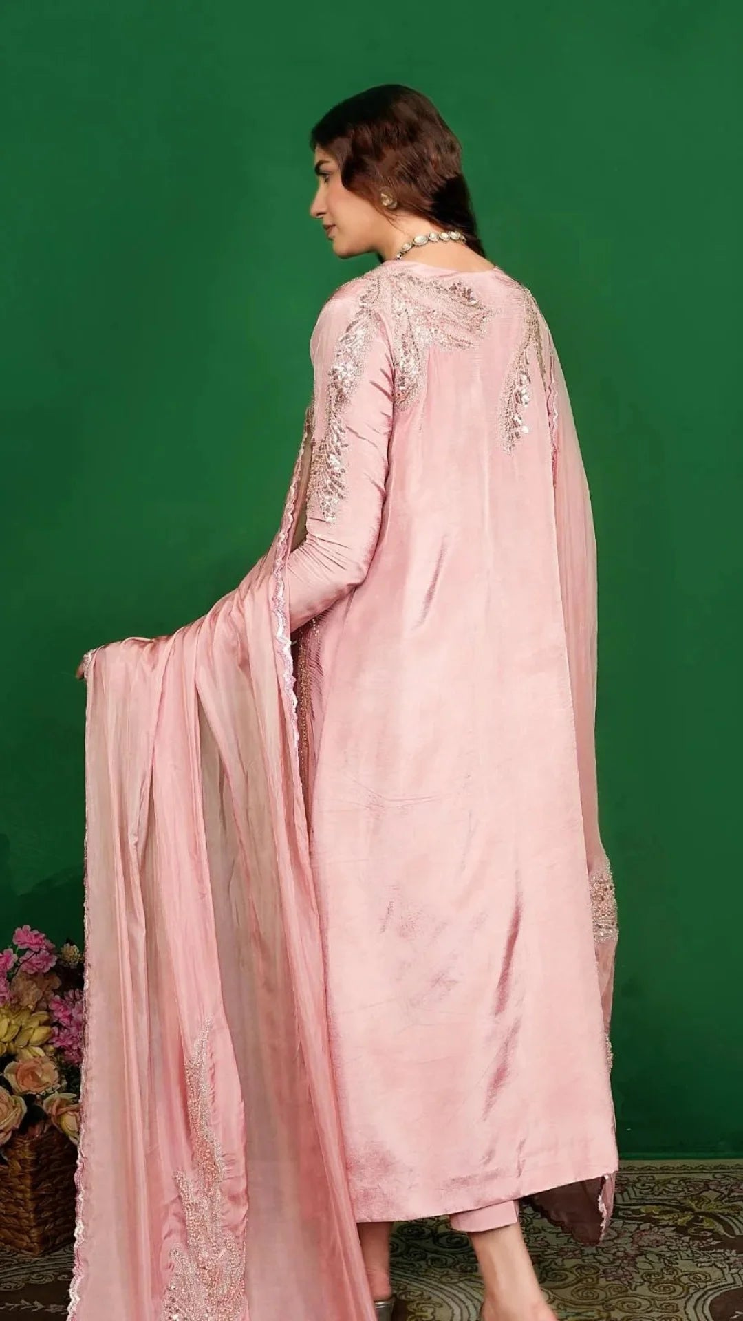 Woman wearing a pink embroidered traditional outfit against a green background
