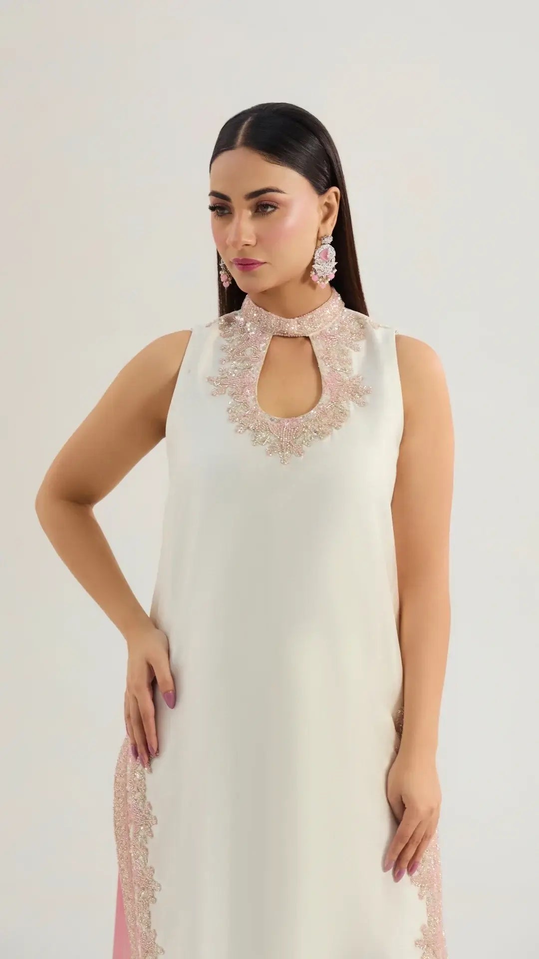 Woman wearing a white dress with floral embellishments on a plain background