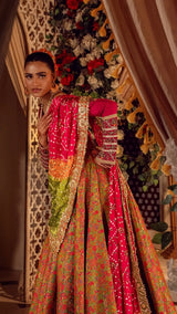 Woman in luxury Pakistani formal wear with red and green embroidered lehenga, floral backdrop