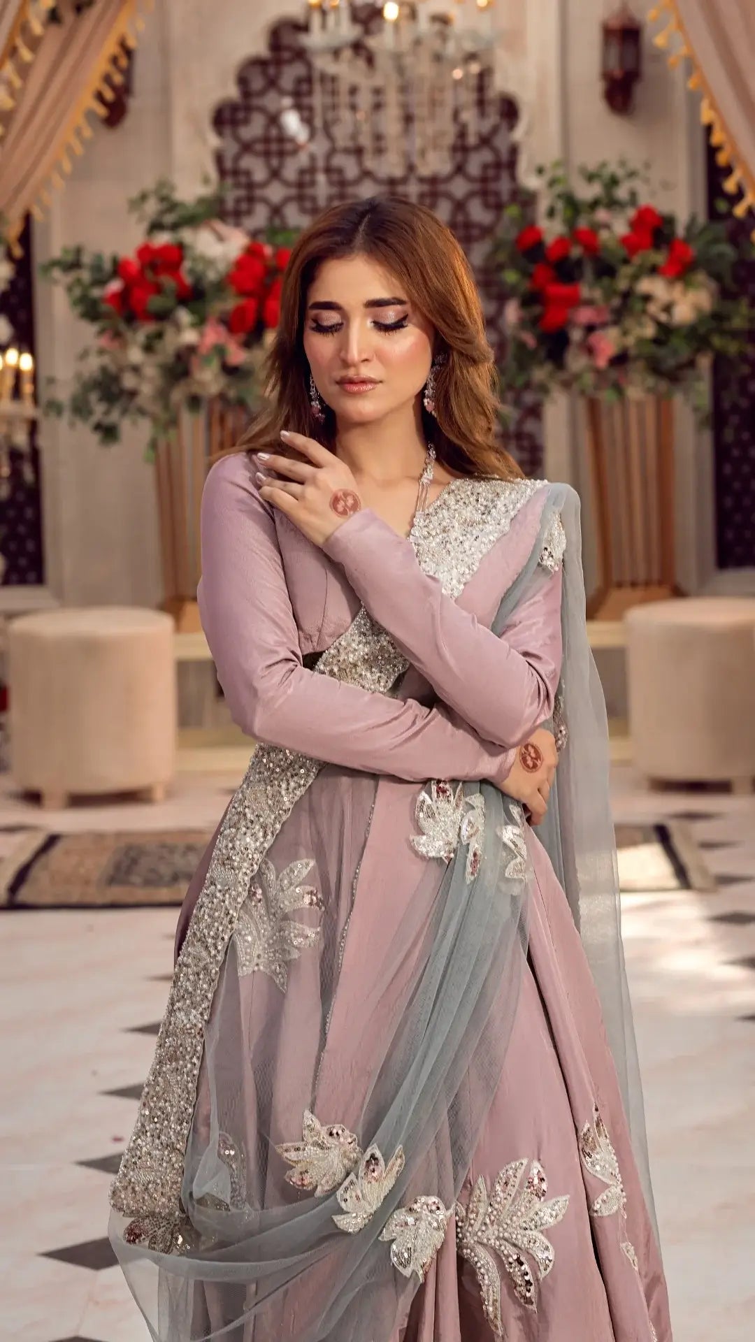 Woman in a pink and gray traditional outfit with floral decorations in an elegant indoor setting.