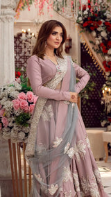 Woman wearing a mauve embroidered Pakistani formal dress with dupatta, floral decor in background