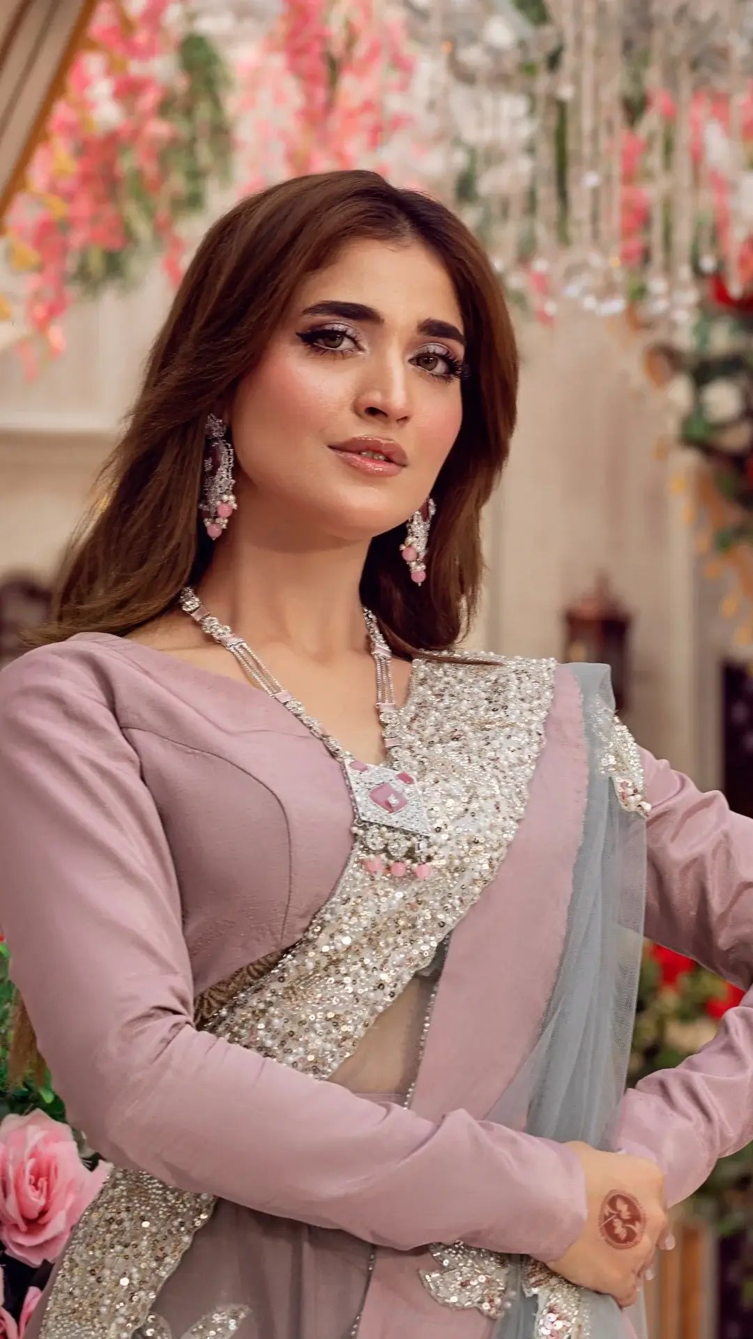 Woman in lilac formal Pakistani dress with silver embellishments, wearing statement jewelry