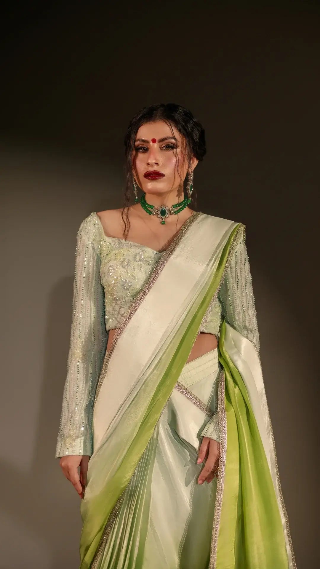 Woman wearing a traditional outfit with a green and white saree against a dark background