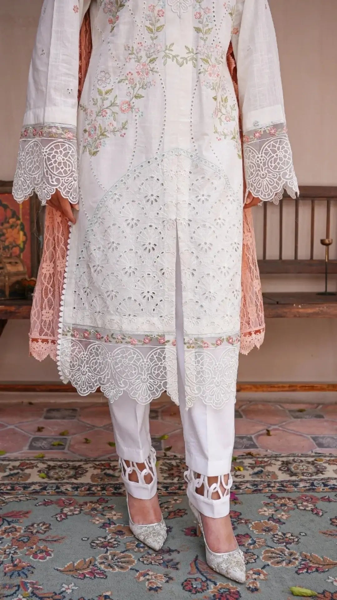 White embroidered traditional outfit with pink accents on a patterned rug.