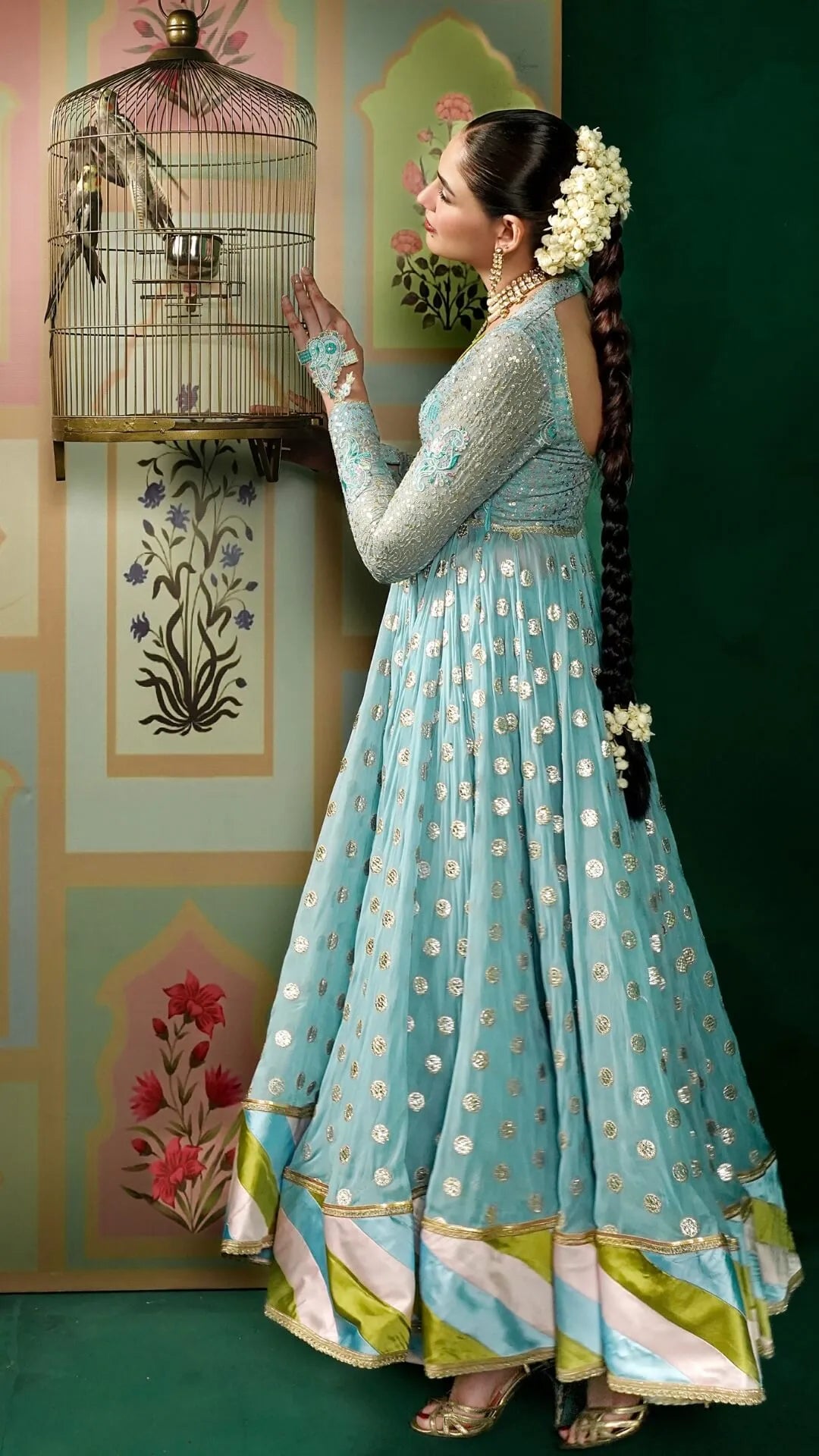 Woman in a light blue traditional outfit with floral decorations, holding a birdcage.