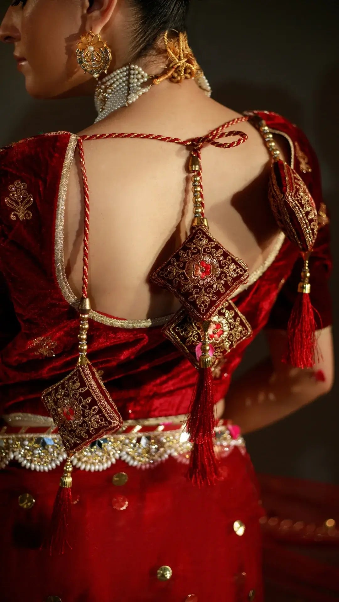 Red embroidered traditional outfit with intricate designs and tassels on a dark background