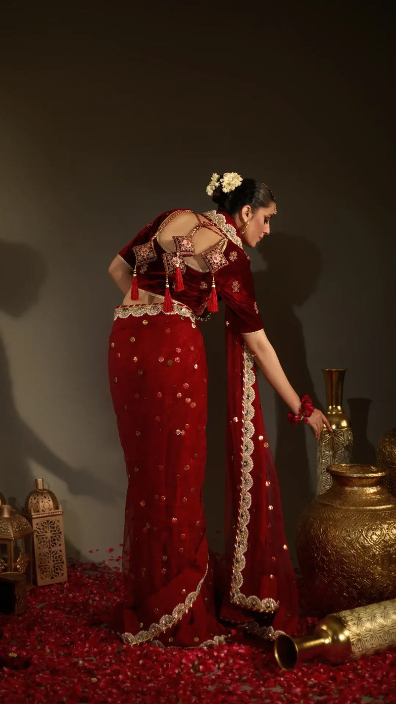 Woman in a red traditional outfit with gold accents, standing next to decorative vases.
