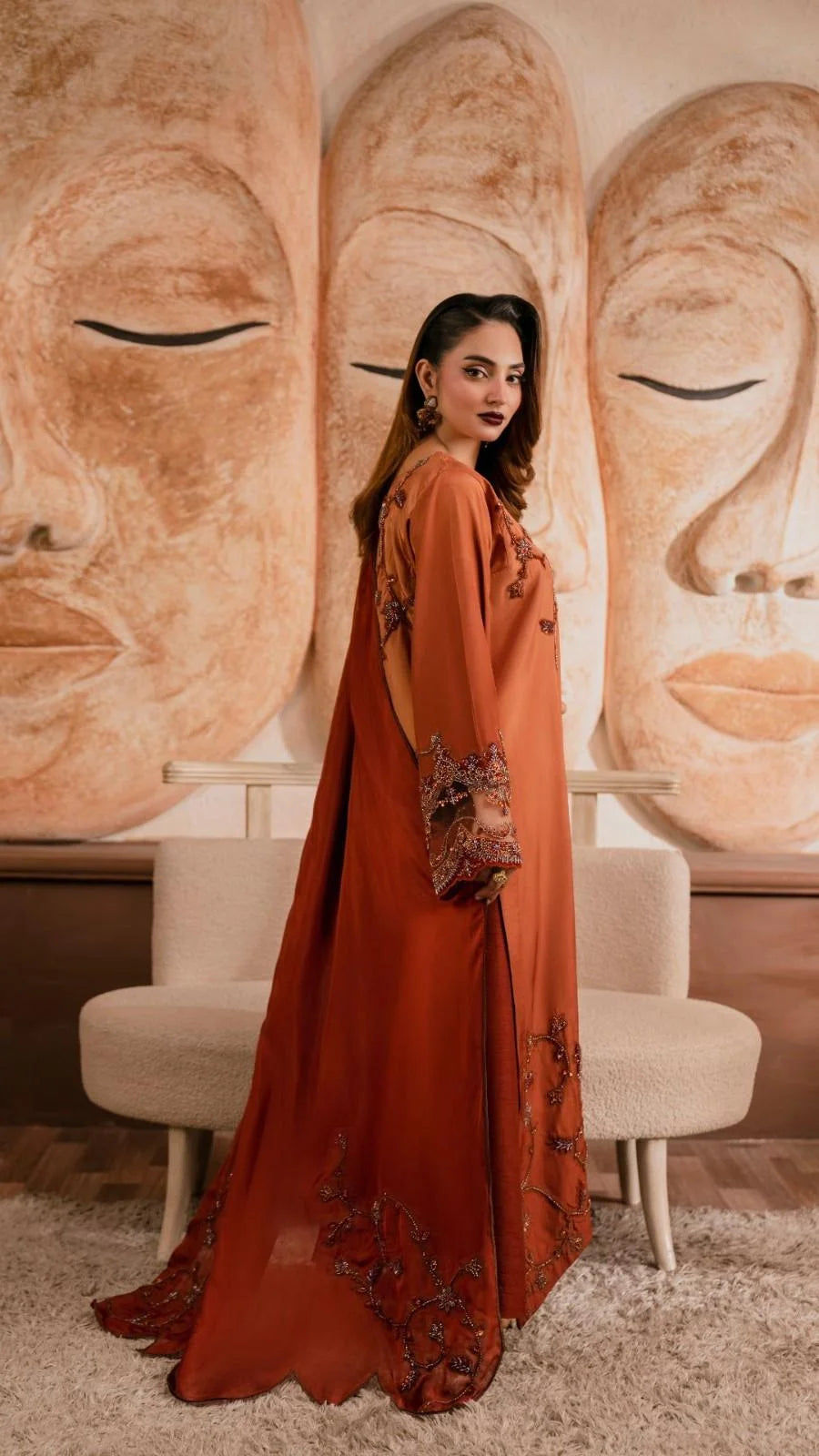 Woman in an orange dress standing in front of large wall art with Buddha faces.