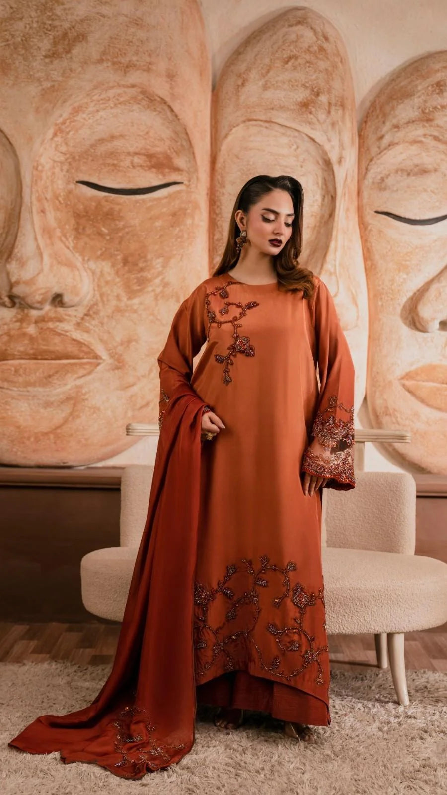 Woman in a rust-colored dress with floral patterns standing in front of Buddha statues.