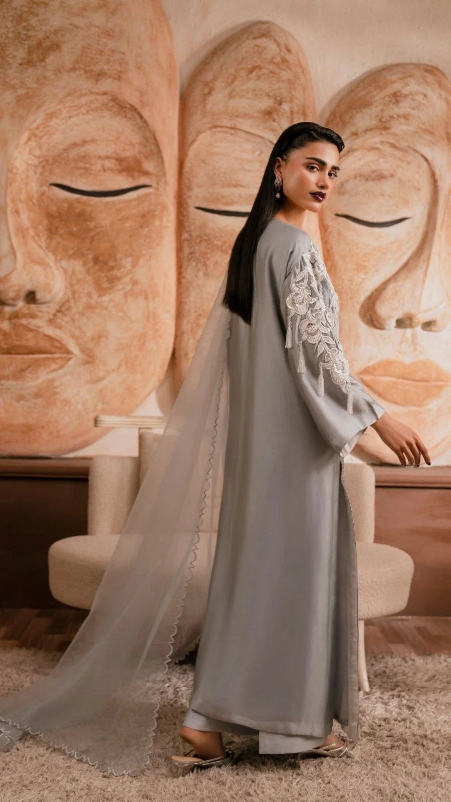 Woman in a gray dress standing in front of a large stone sculpture.