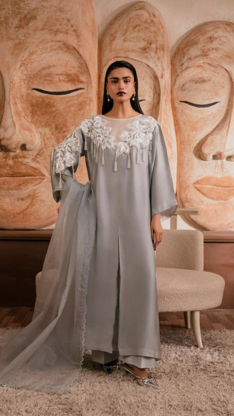 Woman in a gray dress with lace details standing in front of Buddha statues.