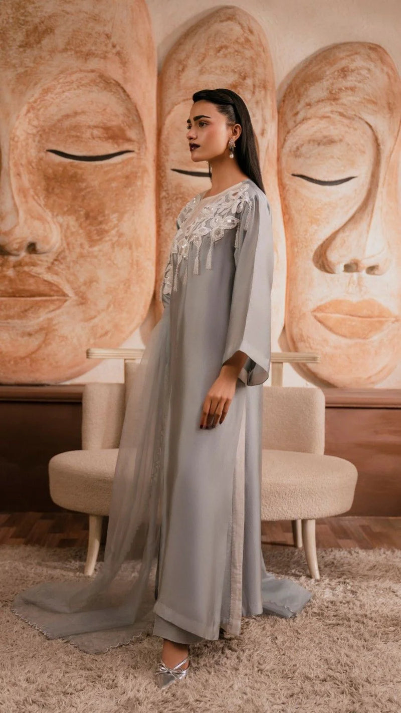 Woman in a long, light gray dress standing in front of Buddha statues.