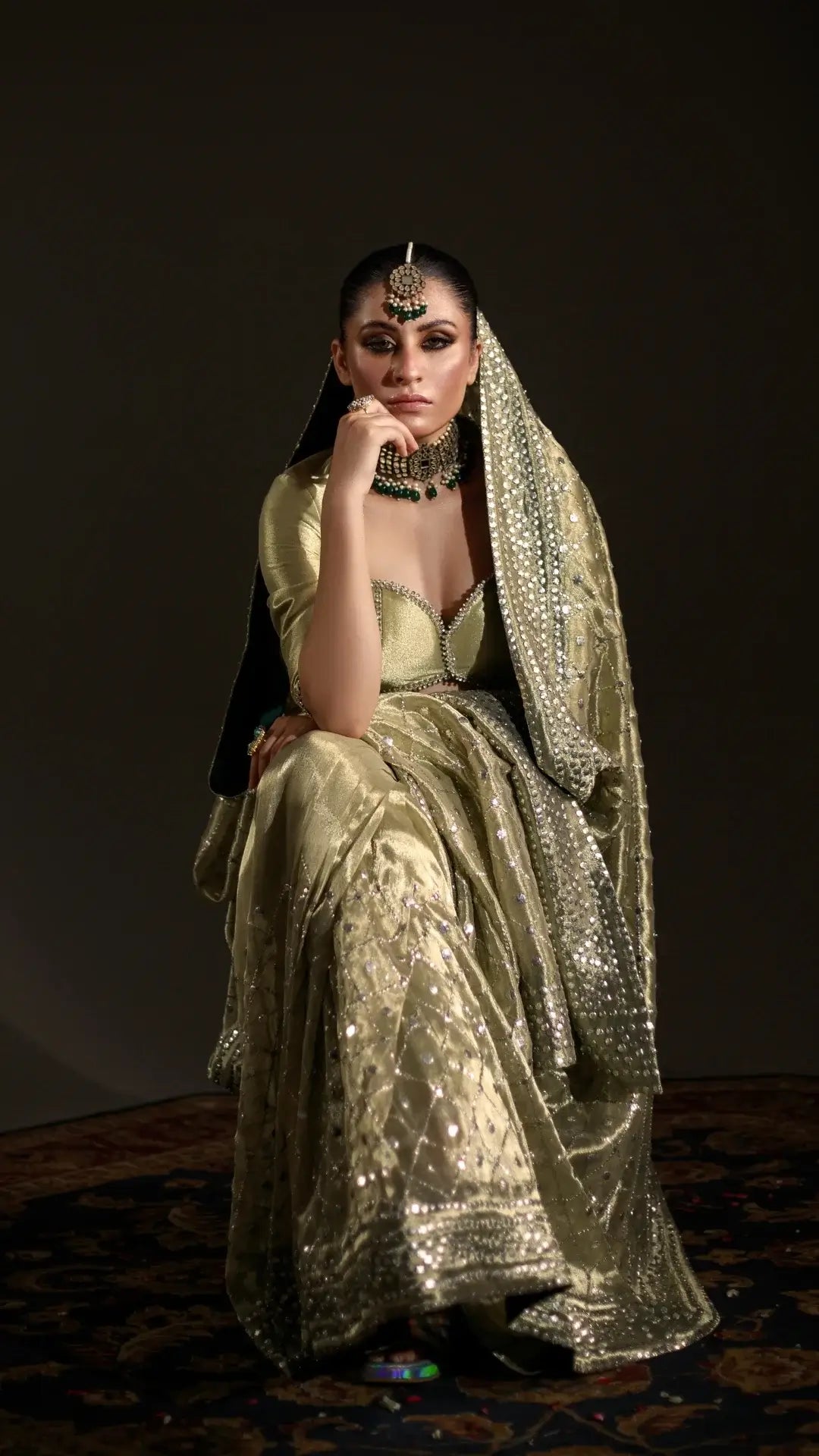 Woman in a gold saree with jewelry against a dark background