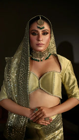 Woman in traditional green and gold outfit with jewelry against a dark background