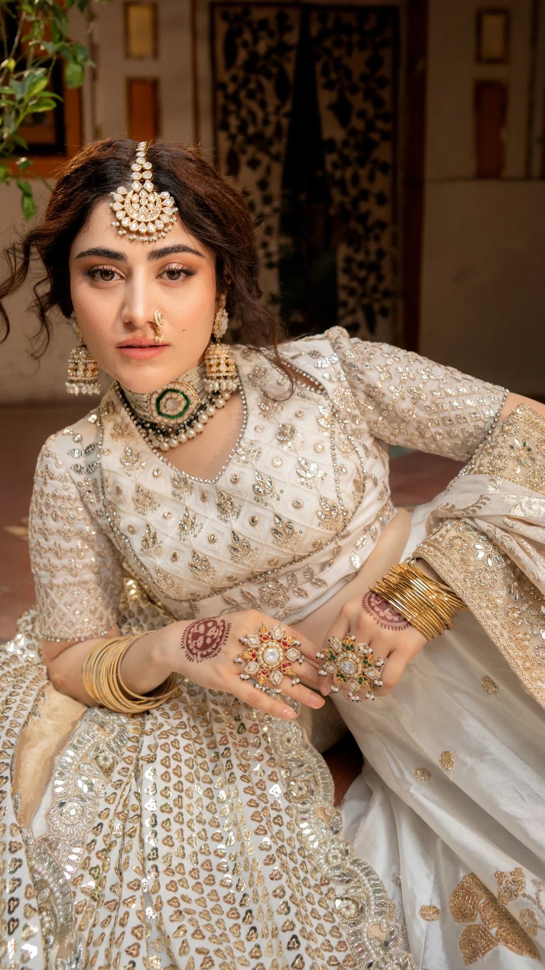Woman in traditional embroidered outfit with jewelry and henna, indoor setting