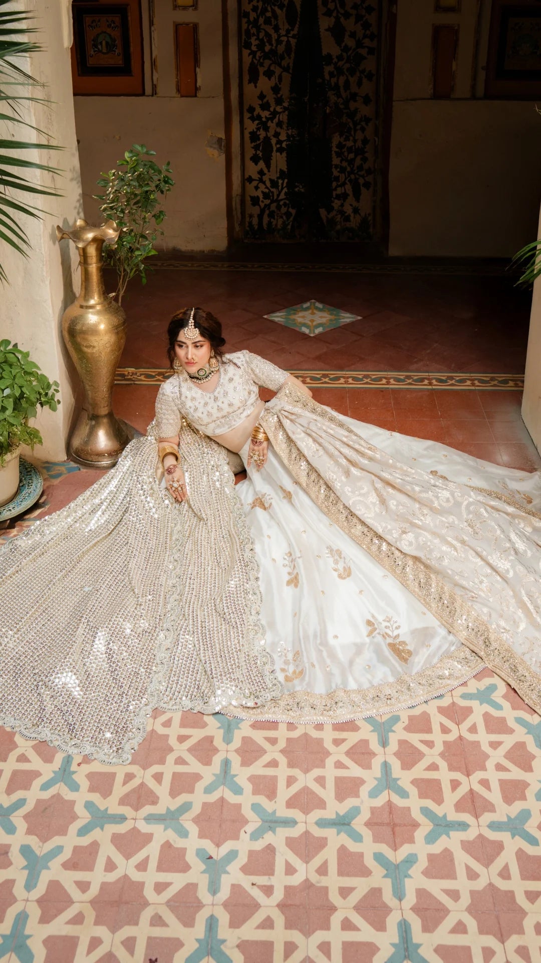Woman in a white and gold embroidered traditional outfit sitting on a patterned floor.