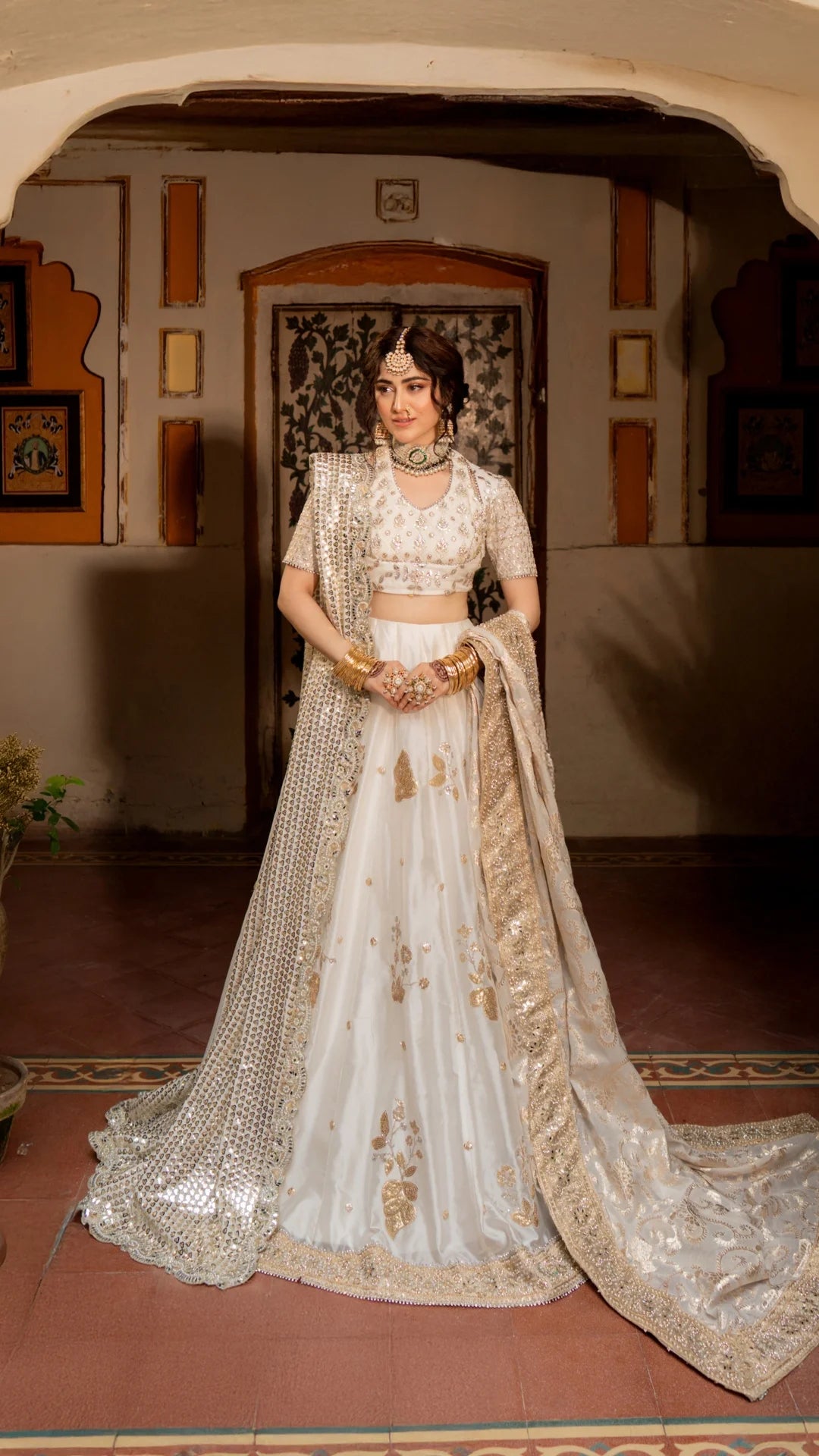 Woman in a traditional white and gold embroidered outfit standing indoors.